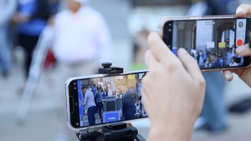 An image with a photo of a person using a cell phone to record a speaker taking the stance.