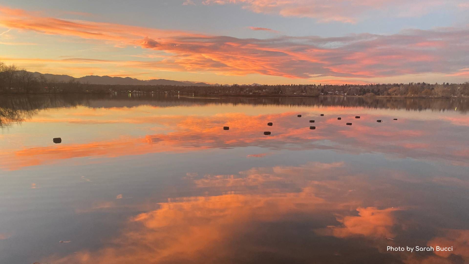 Photograph of a sunset over a lake with bright pink and orange clouds reflected in the water.