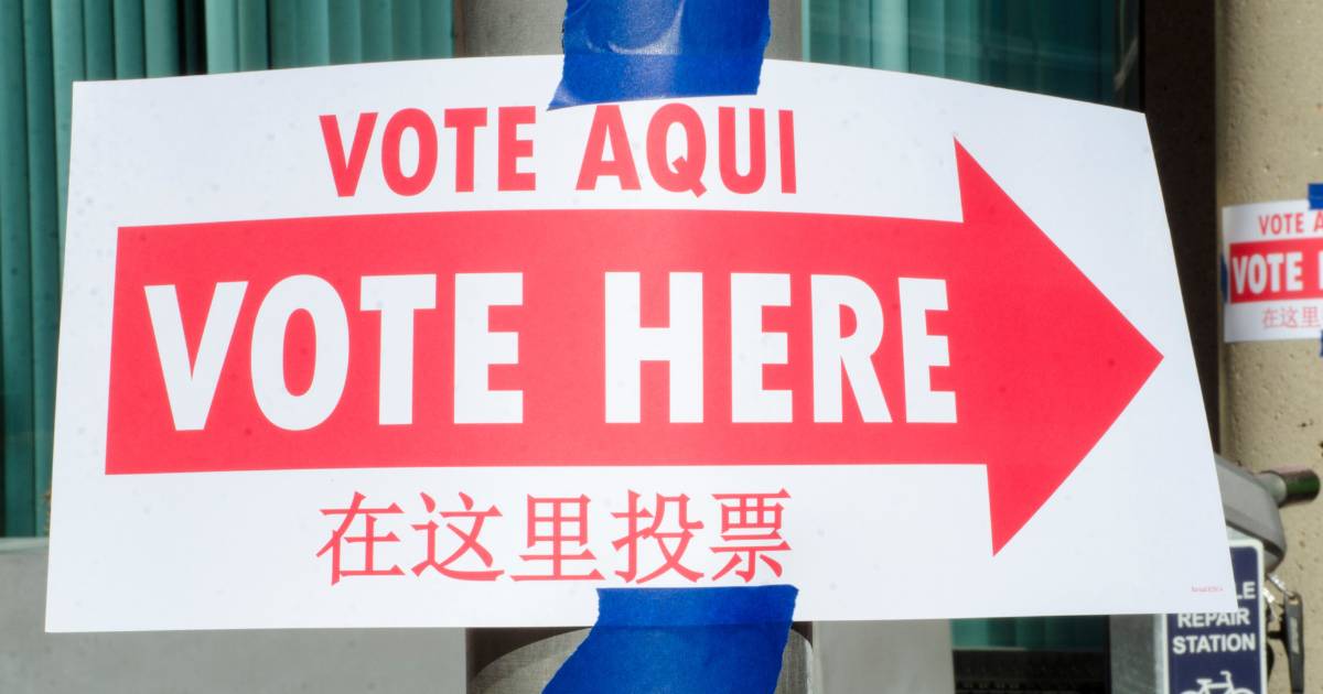 "Vote here" sign taped to a pillar with text in Spanish, English, and Chinese.