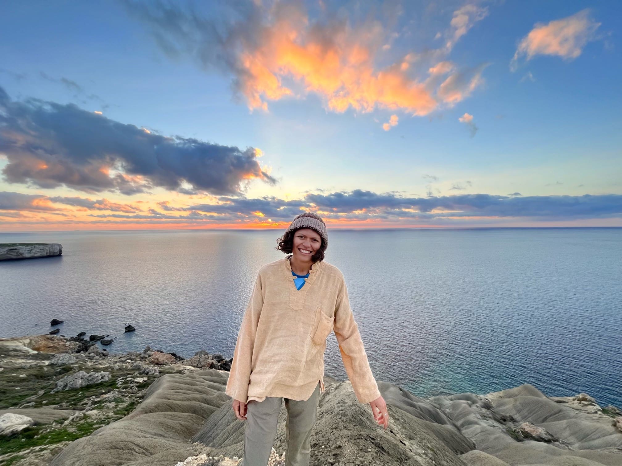 Daela Taeoalii-Tipton smiling and facing the camera at the top of Għajn Ħamiem bluff in Malta at sunset.