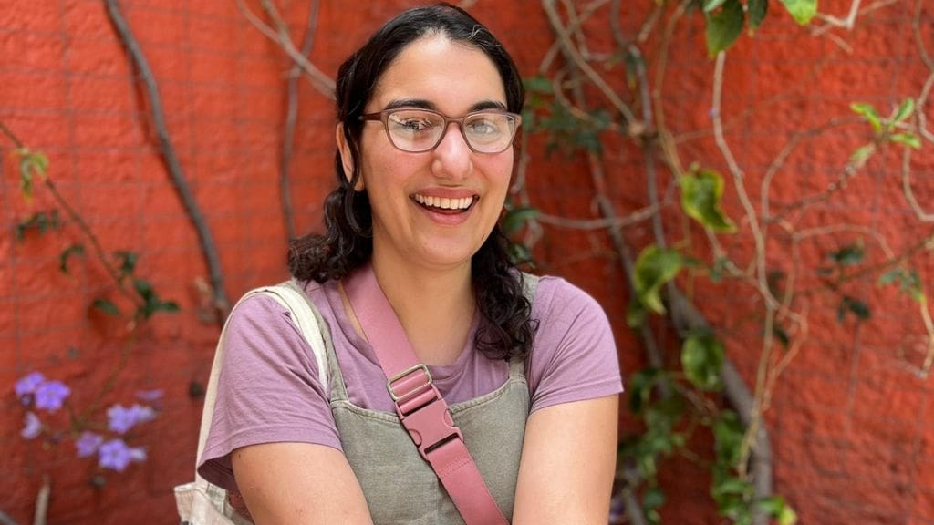 Briana smiles in front of a vibrant red wall that is covered in vines and purple flowers