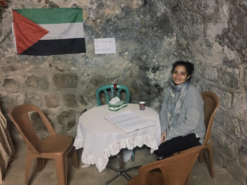 Photo of Sussan sitting at a table with a tea with the flag of Palestine hanging on the wall