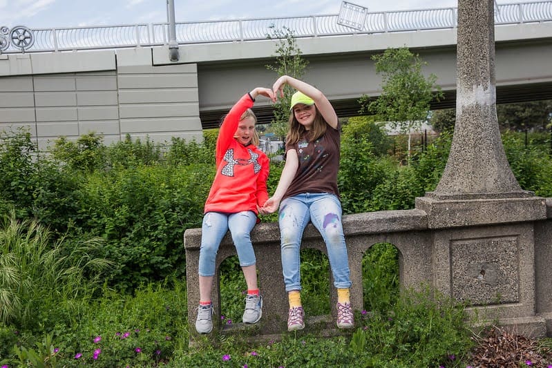 Two children sitting on a concrete wall in the middle of a green stormwater installation in Seattle, surrounded by shrubs and grasses.