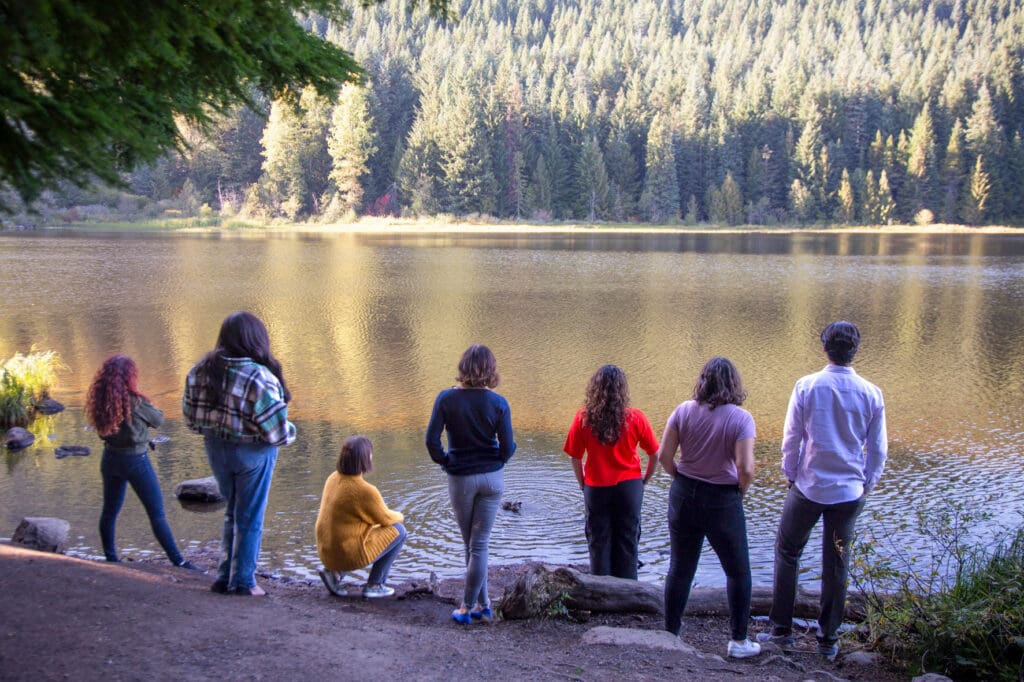 A group shot of the Water Hub team standing on the shore of a lake looking at trees on the horizon