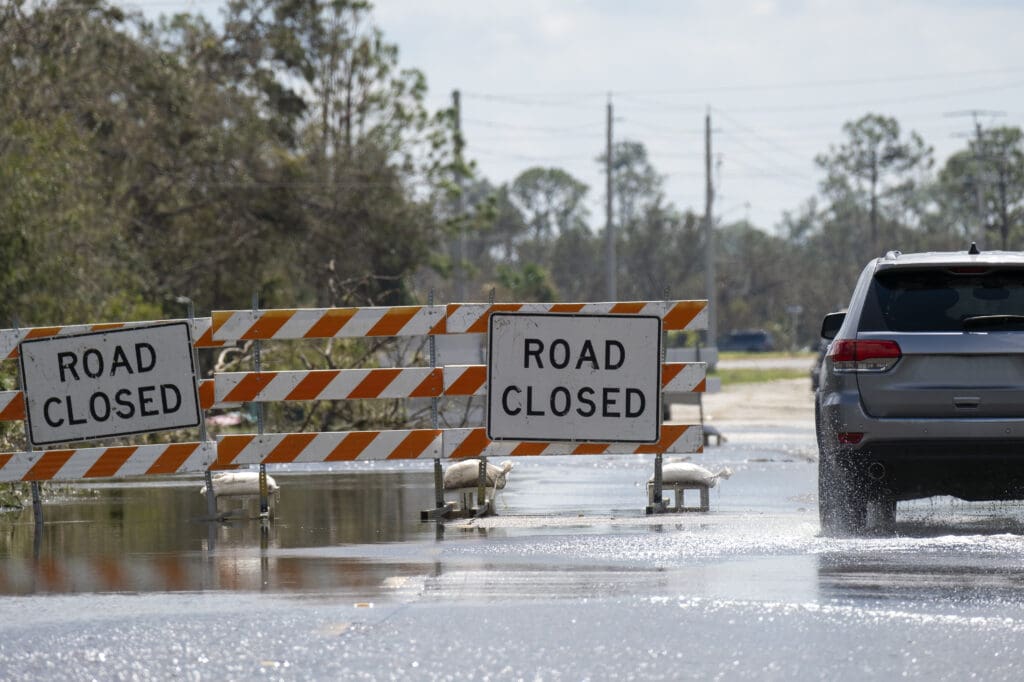 Scene of car driving through flooded street next to "road closed" signage.