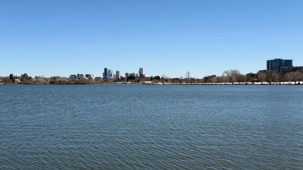 Photograph of a still lake with the Denver city skyline in the background.