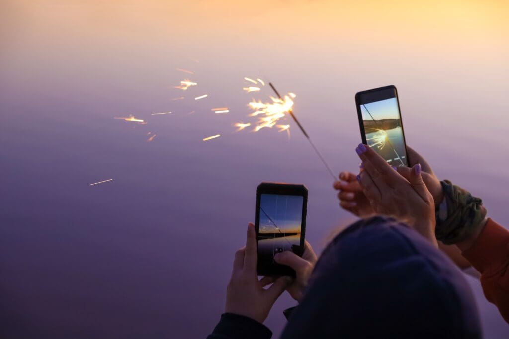Two people take photos of a burning sparkler with their smartphones.