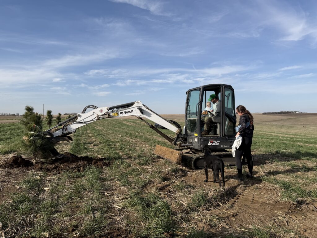an excavator in a field for a tree planting project with a family in the foreground