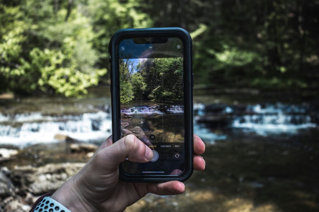 a person holding a cell phone in front of a river